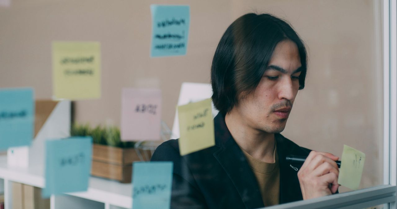 A strategist mapping objectives on a glass wall with sticky notes